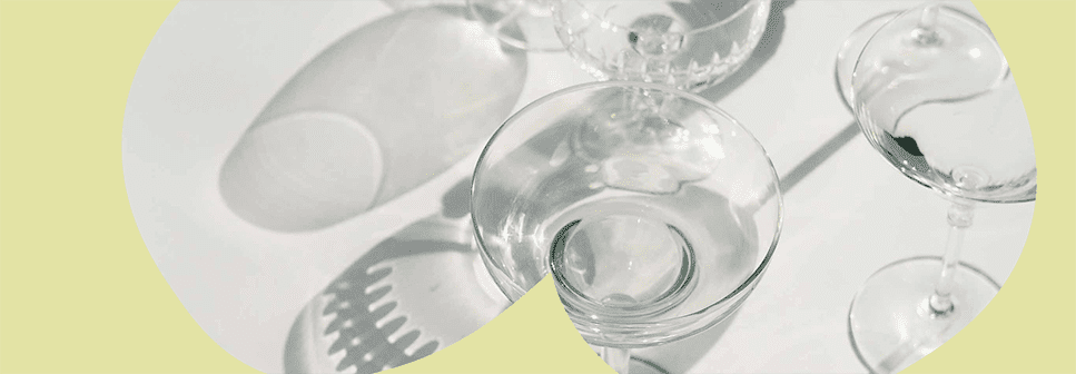 Zdjęcie stojących kieliszków do szampana które rzucają cień na stół z żółtym motywem graficznym na zdjęciu.